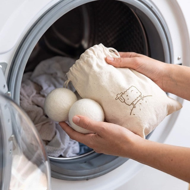 Baabuk wool dryer balls in a natural cotton drawstring bag being placed into a tumble dryer.