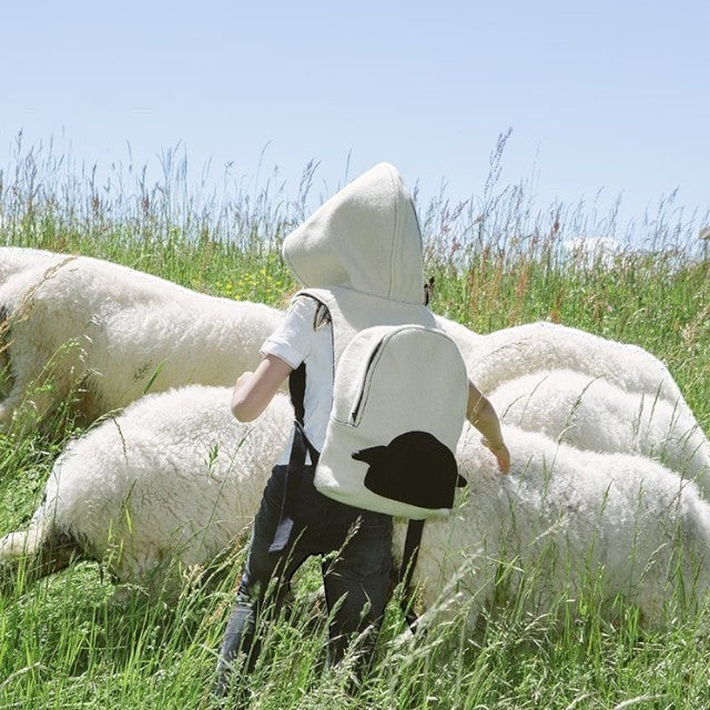 Child wearing a Baabuk wool hooded backpack in a field with Valais Blacknose sheep