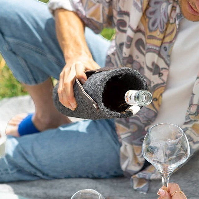 Baabuk dark grey wool wine cooler with leather strap, keeping a bottle chilled outdoors during a picnic.