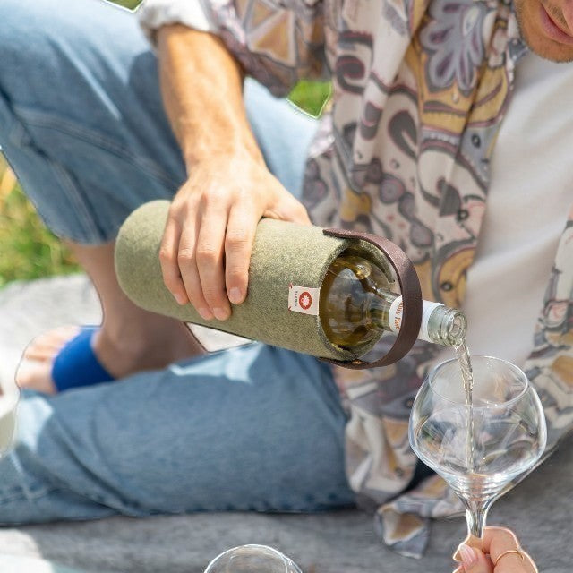 Baabuk khaki green wool wine cooler with a leather strap, being used to pour wine outdoors during a picnic.