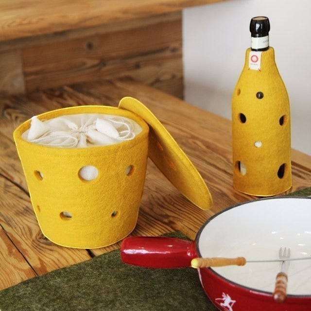 Baabuk yellow felted wool basket with Swiss cheese holes and matching lid on a wooden table with a bottle cover.