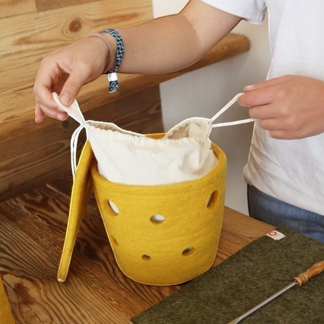 Baabuk small yellow felted wool basket with Swiss cheese-inspired holes and a cream fabric drawstring liner