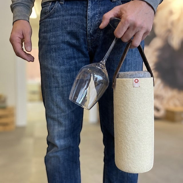 Person holding a yellow Baabuk wool wine cooler with a leather strap and a wine glass in a casual indoor setting.