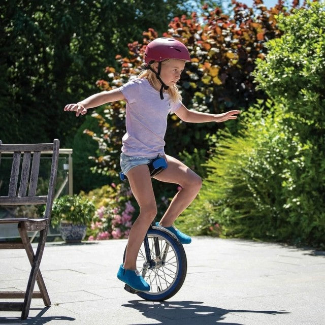 Baabuk Yves Kids slippers in azur blue wool worn by a young girl riding a unicycle outdoors on a sunny day