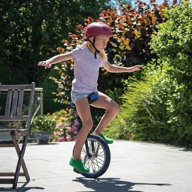 Baabuk Yves Kids emerald green wool slippers worn by a young girl riding a unicycle outdoors