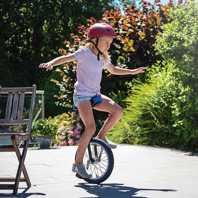 Baabuk Yves Kids light grey wool slippers worn by a girl riding a unicycle outdoors in a sunny garden